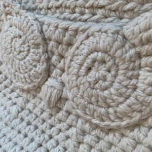May include: Close-up of a beige crocheted fabric with a textured pattern of circles. The fabric is made with thick yarn and has a soft, fuzzy texture.