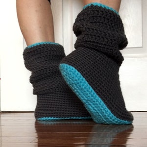 May include: Gray crochet slipper boots with a teal trim. The boots are folded down at the top.