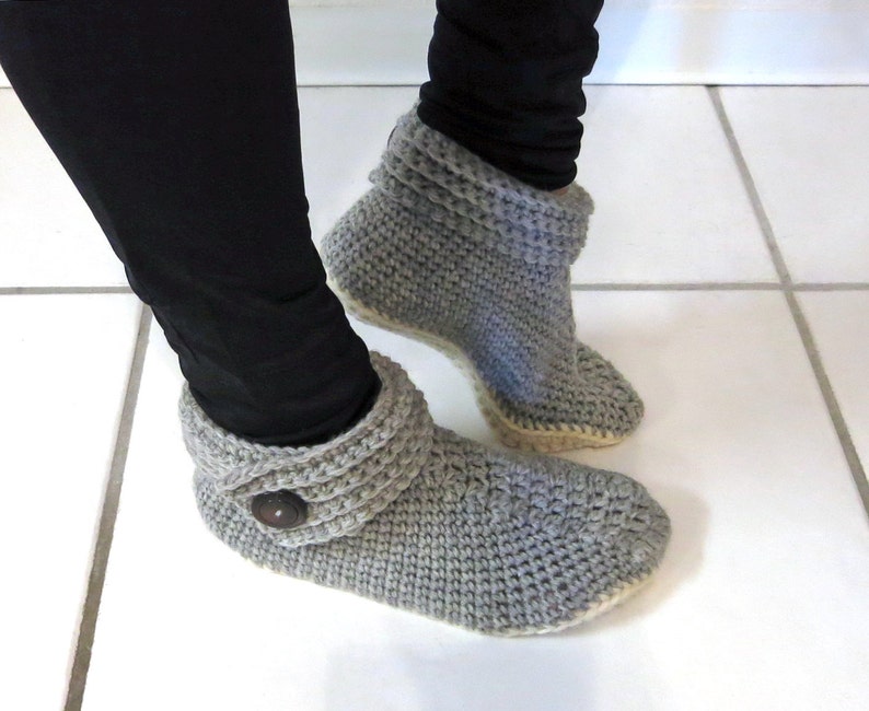 Pu&ograve; includere: Stivali da camera in crochet grigi con polsino ripiegato e dettaglio bottone. Le pantofole hanno una suola bianca.