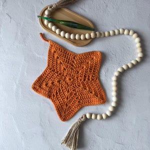 May include: A crocheted orange star with a white tassel hanging from a strand of wooden beads.