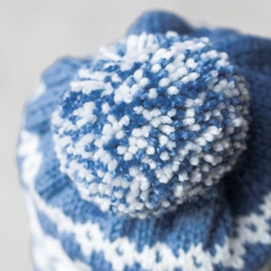 Pu&ograve; includere: Cappello di lana blu e bianco con un pompon soffice in cima.