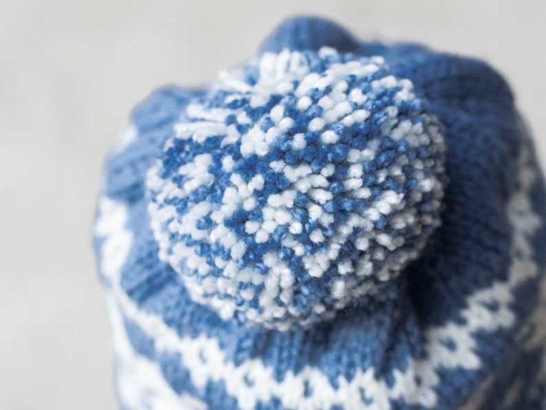 Pu&ograve; includere: Cappello di lana blu e bianco con un pompon soffice in cima.