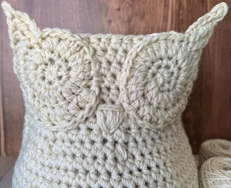 May include: A crocheted owl-shaped basket made of cream-colored yarn. The basket has a large opening and is perfect for storing small items.