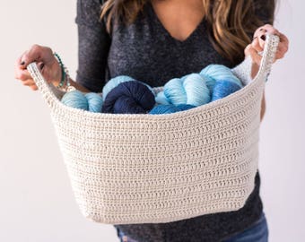 May include: A white crocheted basket with two handles, filled with blue and navy blue yarn balls.