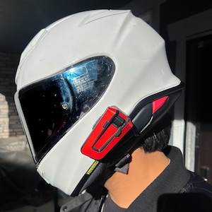 May include: A white motorcycle helmet with a dark visor and a red and black communication device attached to the side. The helmet has a sleek design and appears to be in good condition.