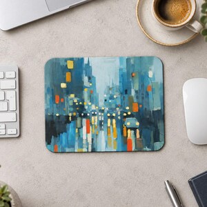 Peut inclure: Un tapis de souris rectangulaire présentant une scène de rue urbaine abstraite peinte dans des tons de bleu, de sarcelle et de gris. L'œuvre représente de hauts bâtiments et une route avec des reflets lumineux jaune et orange vifs.