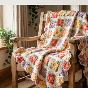 May include: A colourful crochet blanket with a floral design, draped over a wooden chair. The blanket features squares of red, yellow, and purple flowers on a cream background. The edges have a scalloped trim. The chair is made of light-coloured wood.
