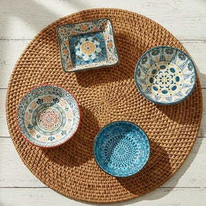 以下が含まれることがあります： 青、オレンジ、白の複雑な模様が施された4つの装飾用セラミックボウルの俯瞰図。ボウルは丸い織りのプレースマットの上に配置されています。ボウルは丸型や四角型など、さまざまな形をしています。