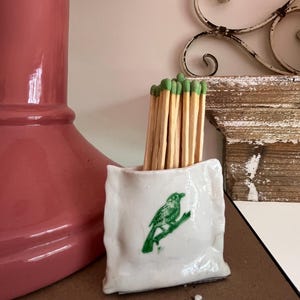 Portacerillas de cerámica verde y blanca con diseño de pájaro. Incluye cerillas decorativas.