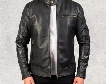 Op de afbeelding: Zwarte leren jas met een opstaande kraag, een ritssluiting aan de voorkant en zakken met ritssluiting. De jas heeft een klassieke bikerstijl met gewatteerde details op de schouders en mouwen. Er wordt een wit T-shirt onder gedragen.