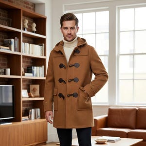 Puede incluir: Un abrigo tipo duffle de color marrón claro con capucha y cierres de palanca. El abrigo tiene dos bolsillos delanteros y se lleva sobre un jersey de cuello alto color crema. El abrigo es de mezcla de lana.