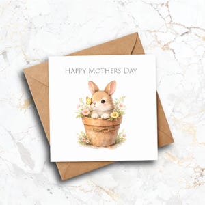 May include: A square greeting card with the text "HAPPY MOTHER'S DAY" features a watercolour illustration of a bunny in a flower pot. The bunny has brown fur and a yellow butterfly. The card is on a brown envelope.
