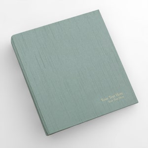 May include: A teal green binder with a textured linen cover. The text "Your Text Here" is printed in gold on the front cover.