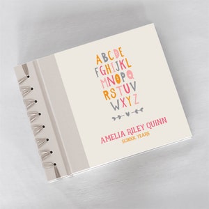 May include: A cream-colored spiral bound book with a colorful alphabet design and the text "Amelia Riley Quinn School Years".