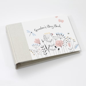 May include: A white book with a linen cover and a colorful floral design on the front. The book says "Grandma's Brag Book" on the front.