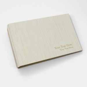 May include: A beige linen-textured photo album with the text "Your Text Here" printed in gold on the front cover.