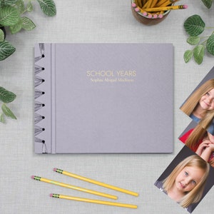 May include: A purple photo album with a spiral binding. The cover has the text "SCHOOL YEARS" and "Sophia Abigail Madison" in gold lettering.