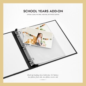 May include: A black and white photo album with clear photo sleeves. The text "SCHOOL YEARS ADD-ON" is at the top. The photo sleeves are designed to hold 5x7 inch photos. A photo of a young girl is inside the sleeve.