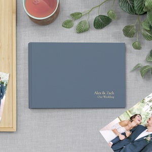 May include: A blue photo album with the text "Alex & Zach Our Wedding" in gold lettering.