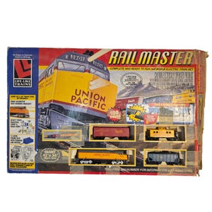 Puede incluir: Un set de tren eléctrico a escala HO Railmaster de Life-Like Trains en su caja original. El empaque muestra una locomotora diésel Union Pacific, un circuito ovalado de 114 cm por 91 cm, e incluye una locomotora, vagones y accesorios.