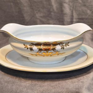 May include: White porcelain gravy boat with a matching saucer. The gravy boat has a scalloped rim and is decorated with gold floral designs. The saucer and boat are trimmed with gold. A classic serving piece.