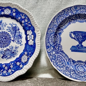 May include: Two decorative ceramic plates with blue and white floral and ornamental designs. One plate has a scalloped edge and a central floral pattern. The other plate features a blue urn design.