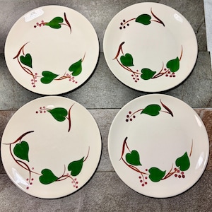 May include: Set of four white ceramic plates with a hand-painted botanical design. Each plate features green leaves, brown stems, and red berry clusters arranged in a circular pattern around the rim. A charming addition to any table setting.