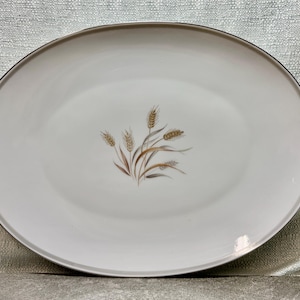 May include: Oval white serving platter with a wheat stalk design in the center. The wheat stalks are in shades of brown, tan, and gold. The rim of the platter has a thin, dark brown border.