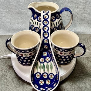 May include: A set of three ceramic mugs with a speckled, matte finish. The mugs are in shades of cream, light gray, and dark gray. Each mug has a simple, minimalist design and a rounded handle. The mugs are stacked on top of each other.
