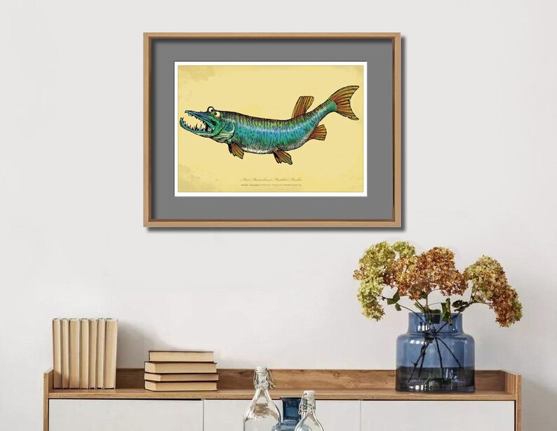 May include: A framed art print featuring a detailed illustration of a fish with sharp teeth and a teal and blue body. The artwork is set against a yellow background and framed in a wooden frame. The print is displayed on a white wall.