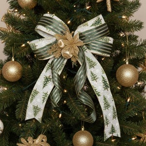 May include: A Christmas tree bow with a gold flower and baubles. The bow has a white ribbon with green Christmas trees and snowflakes, and a green striped ribbon. The baubles are gold.