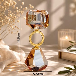 May include: A decorative crystal candle holder, 5.7 inches tall and 2.2 inches wide, with a faceted amber-colored top and base, connected by a gold ring. The candle holder has a gold-colored metal ring and accents.