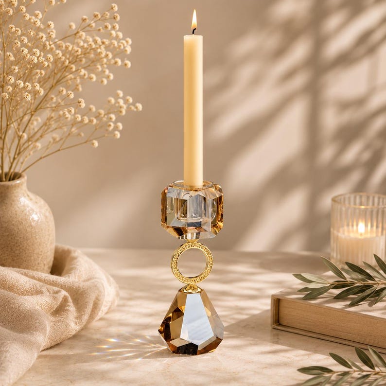 May include: A crystal candle holder with a lit, cream-colored candle. The holder has a geometric design with gold accents and a faceted, teardrop-shaped base. The candle holder is approximately 12 inches tall.