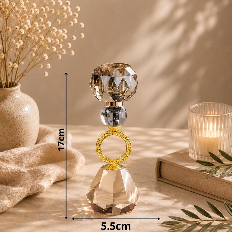 May include: A decorative crystal candle holder with a faceted base and top, connected by a gold ring and a gray crystal sphere. The candle holder is 6.7 inches tall and 2.2 inches wide. The candle holder is designed to hold a single candle.