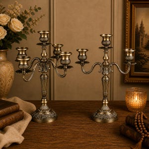 Peut inclure: Deux chandeliers anciens en laiton avec des détails ornés. Chaque chandelier a plusieurs bras pour les bougies, avec une base décorative et des motifs floraux complexes. Les chandeliers sont exposés sur une surface en bois.