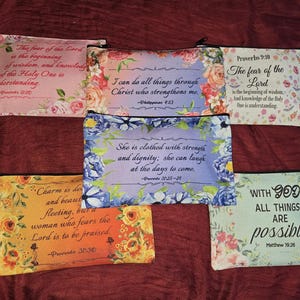 May include: Five rectangular zippered pouches featuring floral patterns and religious text. The pouches display various verses including Proverbs 9:10, Philippians 4:13, Proverbs 31:25-26, Proverbs 31:30, and Matthew 19:26, printed in black script or serif fonts on colorful backgrounds.