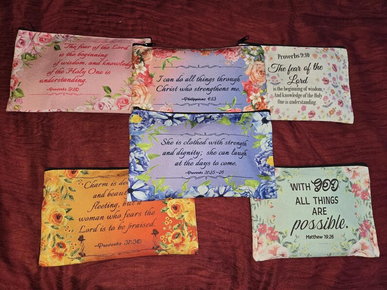 May include: Five rectangular zippered pouches featuring floral patterns and religious text. The pouches display various verses including Proverbs 9:10, Philippians 4:13, Proverbs 31:25-26, Proverbs 31:30, and Matthew 19:26, printed in black script or serif fonts on colorful backgrounds.