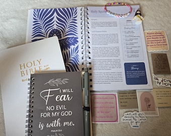 May include: A spiral-bound devotional planner with blue floral patterns, a grey notebook with the text I WILL FEAR NO EVIL FOR MY GOD is with me, a white Holy Bible, a grey pen, a beaded bracelet, a small Jesus figurine, and several religious stickers.