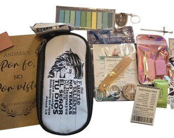 May include: A collection of religious stationery and accessories including a brown notebook with the text 'Andamos por fe, no por vista', a white pencil case with a lion graphic and Spanish text, a sword-shaped pin, stickers, and a receipt.