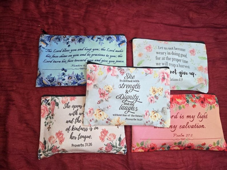 May include: Five rectangular zippered pouches featuring floral patterns and printed Bible verses. The pouches display various color schemes including blue, pink, and white, with black text detailing scriptures such as Proverbs 31:25 and 31:26.