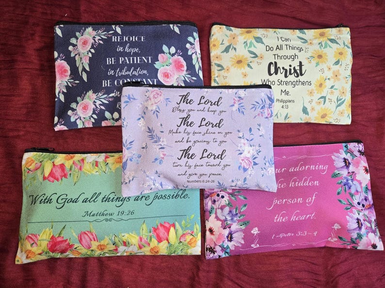 May include: Five rectangular zippered pouches featuring floral patterns and religious text. The pouches are navy blue, yellow, light purple, mint green, and pink. Each displays a unique scripture verse printed in black, decorative script and serif fonts.