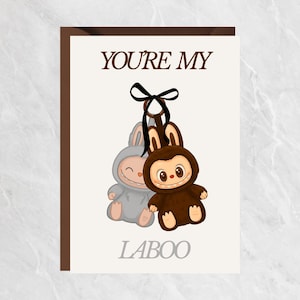以下が含まれることがあります： 茶色の縁取りのグリーティングカード。茶色で「YOU'RE MY」、グレーで「LABOO」の文字が書かれています。2匹の漫画のウサギのイラストがあり、1匹はグレー、もう1匹は茶色で、黒いリボンが付いています。