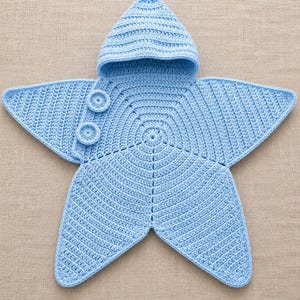 May include: A light blue star-shaped crochet blanket featuring a pointed hood at the top and two circular buttons on the side. The garment is constructed with a consistent ribbed stitch pattern throughout, forming five distinct points in a star shape.