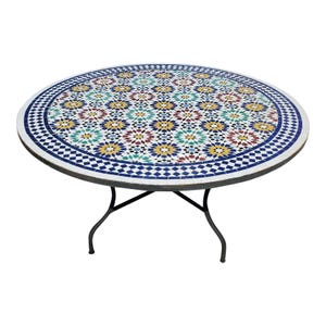 May include: Round mosaic tile table with a colourful floral pattern in shades of blue, yellow, red, and green. The table has a dark metal frame and legs. The table is approximately 122 cm in diameter.