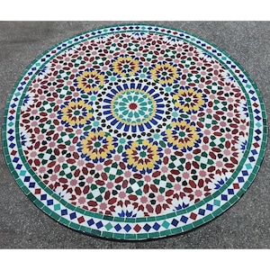 May include: A round mosaic table with a colorful geometric pattern. The table features a central design of blue, yellow, and red shapes, surrounded by a border of green and white tiles. The table is approximately 48 inches in diameter.