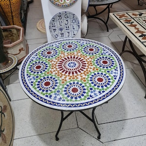 Op de afbeelding: Ronde mozaïek tegel tafel met een zwart metalen onderstel. Het tafelblad heeft een kleurrijk geometrisch patroon in tinten rood, blauw, groen en oranje. De tafel heeft een diameter van ongeveer 61 cm.