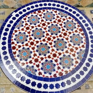 May include: Round mosaic tile table with a detailed geometric pattern in shades of blue, red, gray, and white. The table has a dark edge and a decorative border of blue stars. The table's diameter is approximately 30 inches.