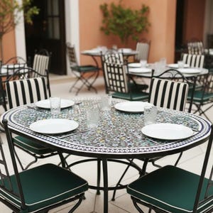 May include: An outdoor dining set featuring a mosaic tile table and black metal chairs. The chairs have dark green cushions with white piping and black and white striped backs. White plates and glasses are set on the table, ready for a meal.