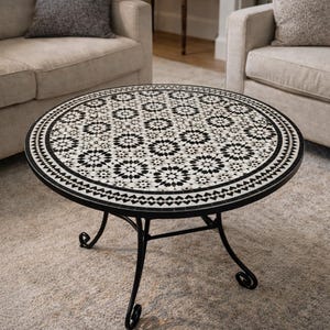 May include: A round coffee table with a black metal frame and a mosaic tile top. The tile design is a repeating pattern of black and white geometric shapes. The table has decorative, scrolled legs.