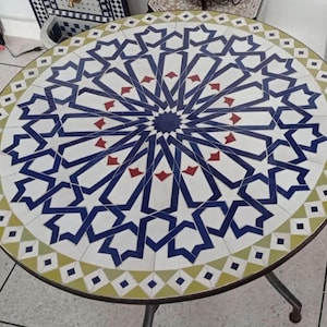 Op de afbeelding: Ronde mozaïek tafel met een geometrisch sterrenpatroon in blauw, wit en rood. De tafel heeft een donker metalen frame en een rand van groene en gele ruitvormen. Geschikt voor terras of binnenruimte, diameter ongeveer 75 cm.